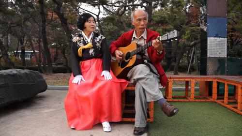 A scene from the movie. An old lady is singing a song in accordance with guitar playing.