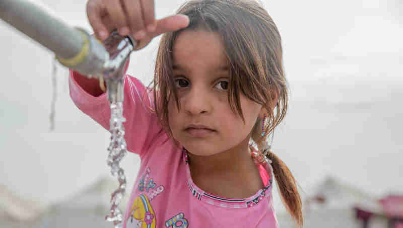 A young girl from Mosul takes water from a tap stand at a UNICEF-supported Temporary Learning Space in Hassan Sham Displacement Camp, Ninewa Governorate. "I like it here because we've been out of school for two years," she said. Photo: UNICEF