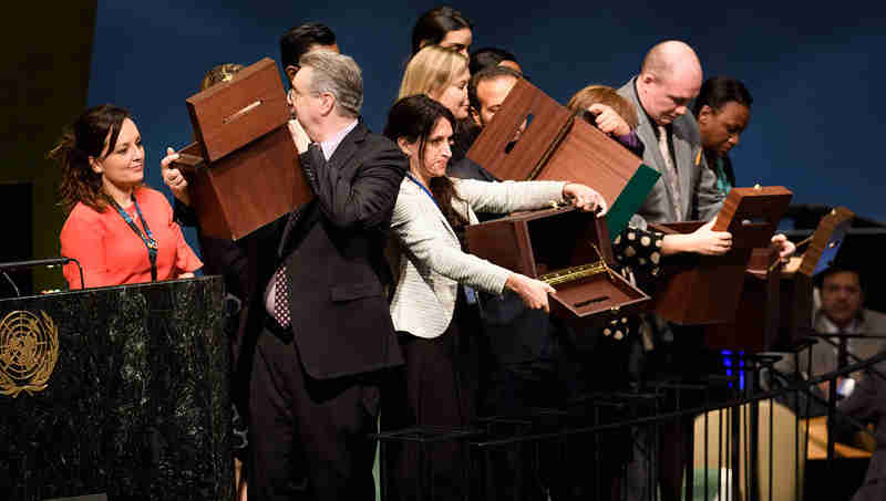 Conference officers hold up empty ballot boxes before collecting ballots from delegates. UN Photo/Manuel Elias