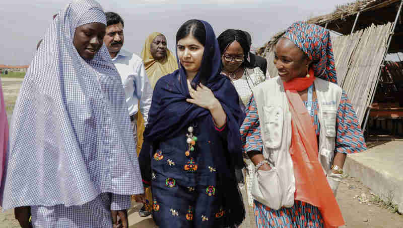 On 18 July 2017 in Maiduguri, Malala Yousafzai (center) is shown around the school in Bakassi camp by student, Fatima Grema (left) who has been displaced by the conflict in northeast Nigeria. During her visit to Nigeria, education activist Malala Yousafzai met with girls displaced by the Boko Haram crisis.