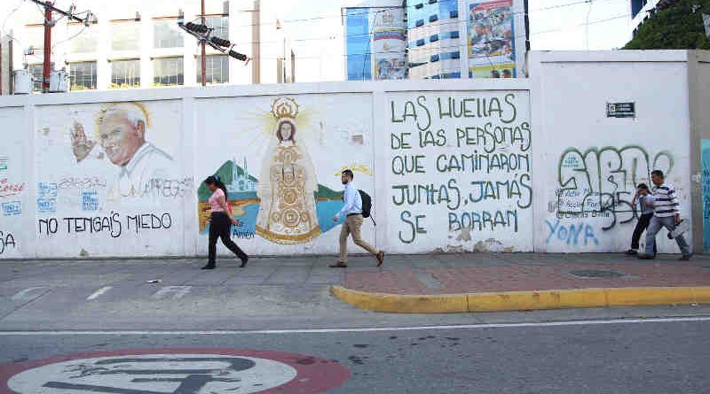 3 June 2019: People pass in front of street graffiti in Caracas, Venezuela. The text reads: “The footprints of those who travel together will never be erased.” Photo: UNICEF